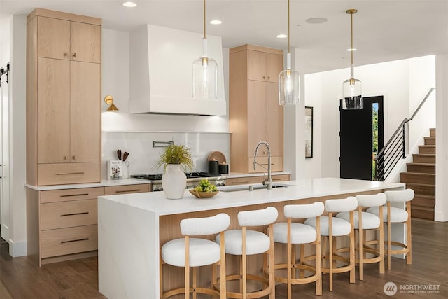 kitchen featuring light brown cabinetry, a sink, wall chimney range hood, light countertops, and dark wood-style floors