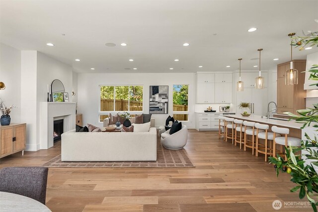 living area featuring recessed lighting, light wood-type flooring, and a warm lit fireplace