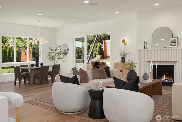 living room with wood finished floors, recessed lighting, a warm lit fireplace, and a chandelier