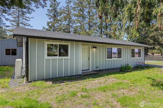 view of front of property with board and batten siding, a front yard, roof with shingles, ac unit, and fence