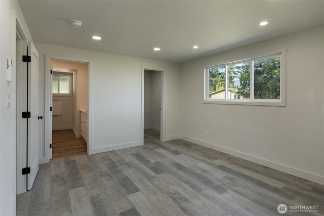unfurnished bedroom featuring baseboards, recessed lighting, wood finished floors, and a walk in closet