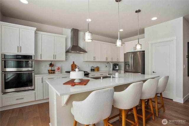 kitchen featuring wall chimney range hood, backsplash, appliances with stainless steel finishes, a sink, and light countertops