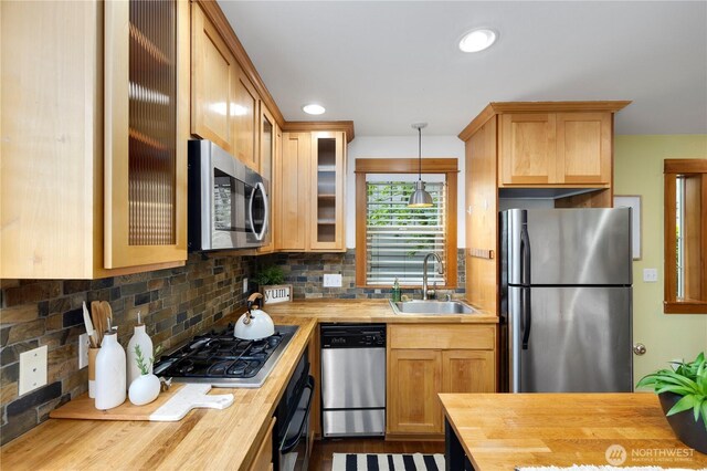 kitchen featuring a sink, appliances with stainless steel finishes, tasteful backsplash, and wooden counters
