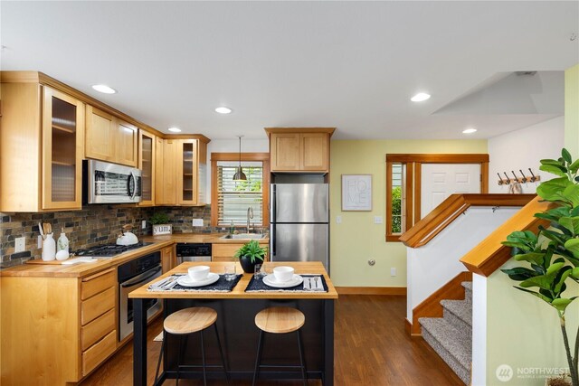 kitchen with decorative backsplash, dark wood-style flooring, a breakfast bar, baseboards, and stainless steel appliances