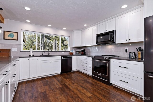kitchen featuring dark countertops, a sink, black appliances, backsplash, and white cabinetry