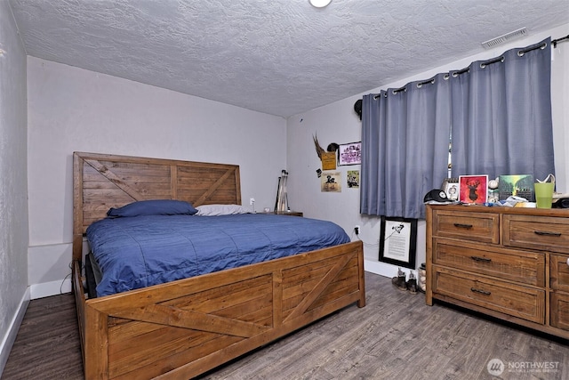 bedroom featuring baseboards, wood finished floors, visible vents, and a textured ceiling
