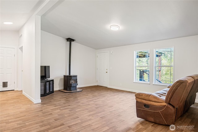 living area with baseboards, a wood stove, and light wood finished floors