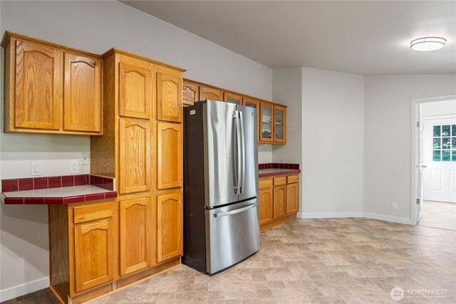 kitchen featuring brown cabinets, freestanding refrigerator, tile countertops, and glass insert cabinets