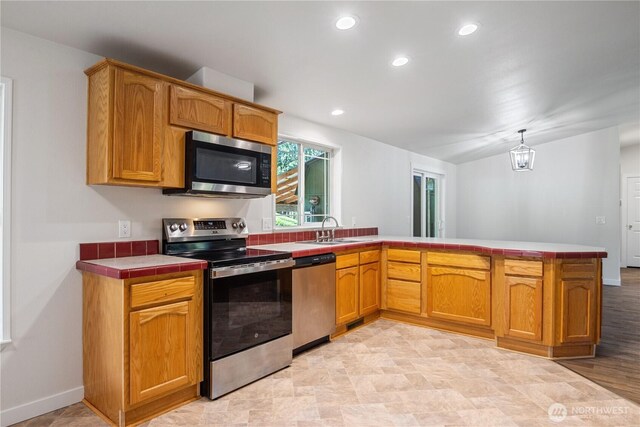 kitchen with tile counters, recessed lighting, stainless steel appliances, a sink, and a peninsula
