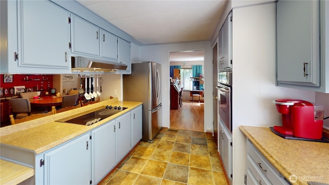 kitchen with stone finish flooring, under cabinet range hood, appliances with stainless steel finishes, and light countertops