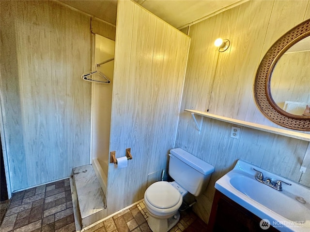 bathroom featuring toilet, wood walls, a shower, vanity, and brick patterned floor