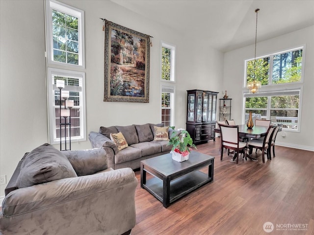 living room with baseboards, a high ceiling, dark wood-style flooring, and a chandelier