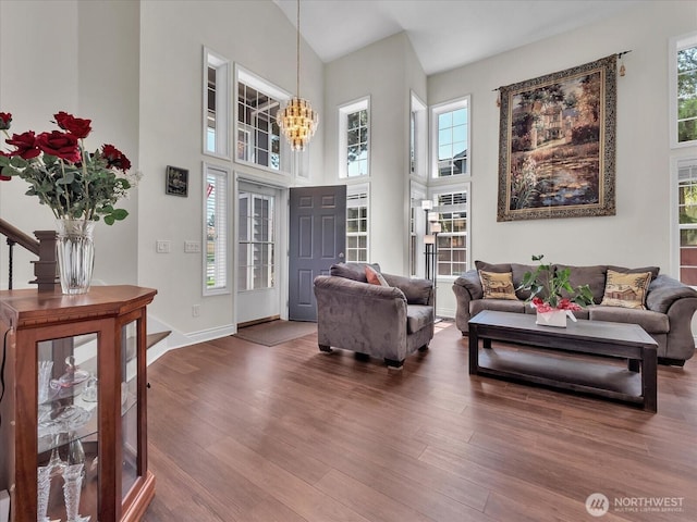 living area with an inviting chandelier, baseboards, wood finished floors, and high vaulted ceiling