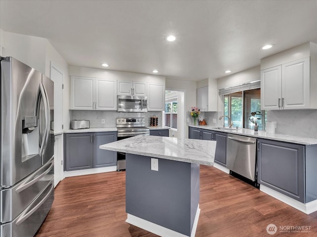 kitchen with a sink, gray cabinets, stainless steel appliances, backsplash, and a kitchen island