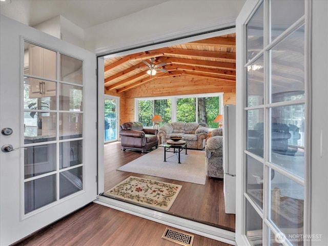 living area featuring wooden walls, vaulted ceiling with beams, wood finished floors, and visible vents