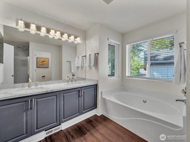 bathroom featuring double vanity, a garden tub, visible vents, wood finished floors, and a sink
