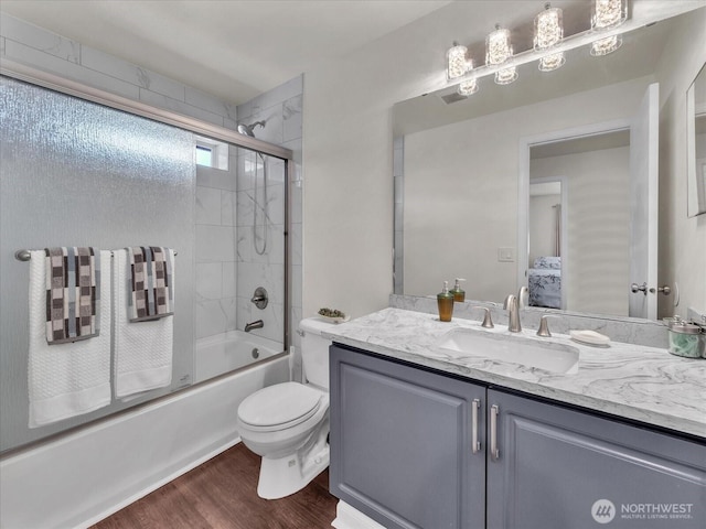 bathroom with toilet, wood finished floors, bath / shower combo with glass door, and vanity
