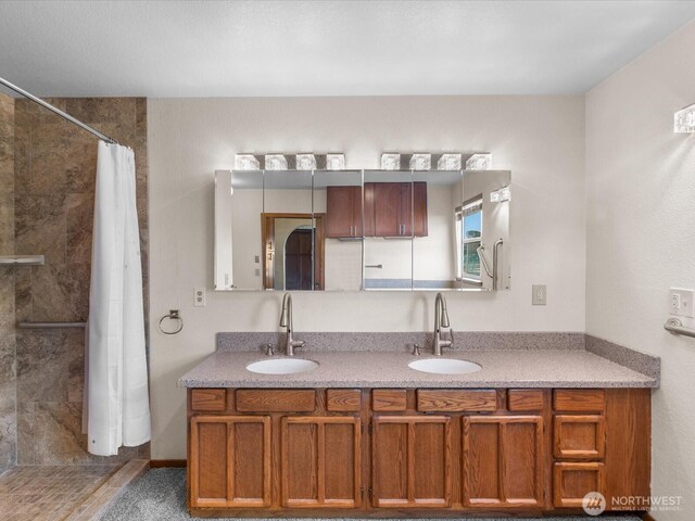bathroom featuring a tile shower, double vanity, and a sink
