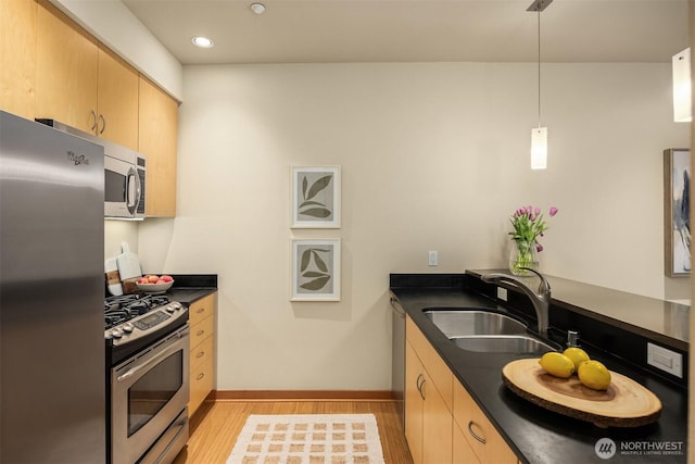 kitchen featuring dark countertops, appliances with stainless steel finishes, a sink, light brown cabinets, and light wood-type flooring