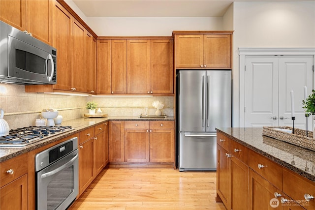 17288 NE 120th Way, Redmond, WA 98052 - kitchen with dark stone countertops, appliances with stainless steel finishes, brown cabinetry, and light wood-style floors