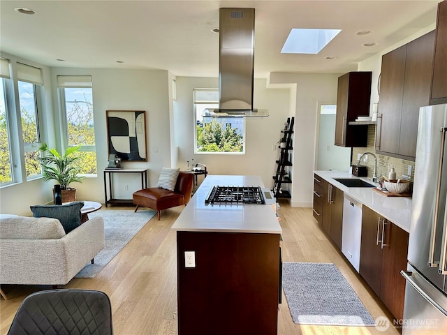 kitchen with appliances with stainless steel finishes, a sink, light countertops, open floor plan, and a skylight