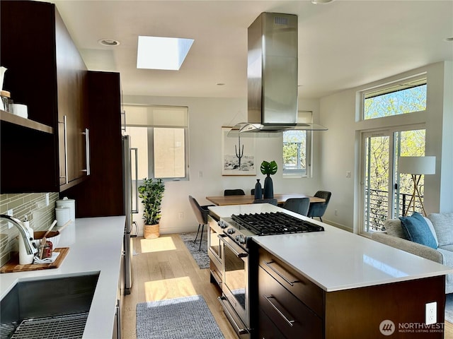 kitchen featuring appliances with stainless steel finishes, a sink, light wood-style floors, island exhaust hood, and a skylight