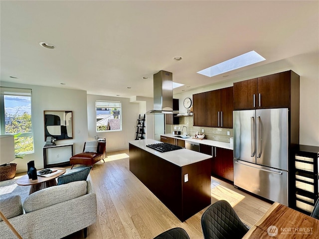 kitchen featuring island range hood, a skylight, light countertops, open floor plan, and stainless steel appliances