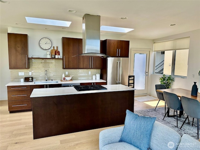 kitchen with island exhaust hood, a skylight, high quality fridge, light countertops, and a sink
