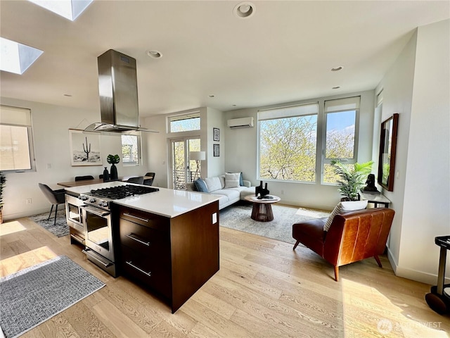 kitchen with a wall unit AC, island exhaust hood, light wood finished floors, stainless steel range with gas stovetop, and a skylight