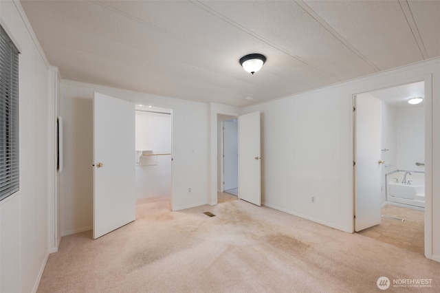 unfurnished bedroom featuring a walk in closet, baseboards, ensuite bath, and light colored carpet