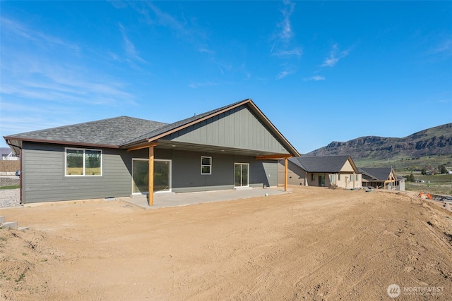 rear view of property featuring roof with shingles, a mountain view, and a patio area