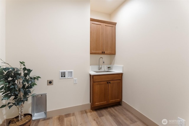 laundry room featuring cabinet space, electric dryer hookup, a sink, light wood finished floors, and washer hookup