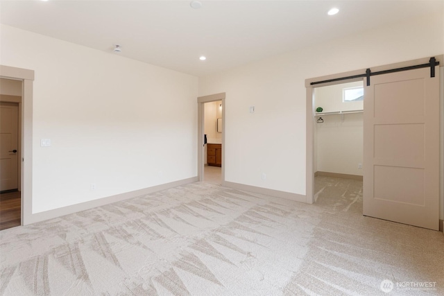 unfurnished bedroom with light colored carpet, a barn door, baseboards, a spacious closet, and recessed lighting