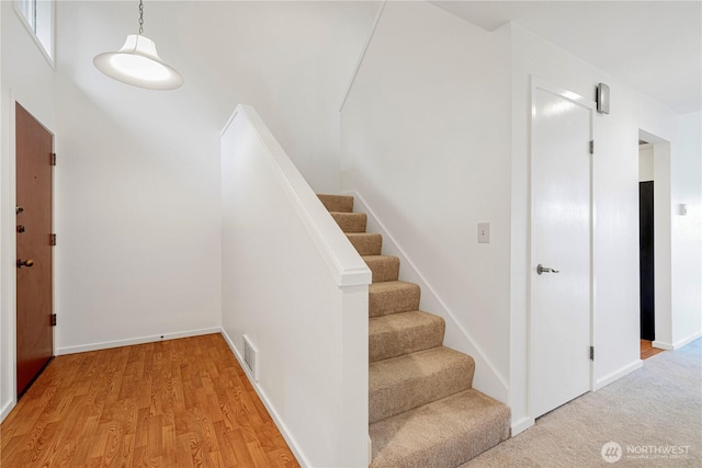 stairway featuring wood finished floors, visible vents, and baseboards
