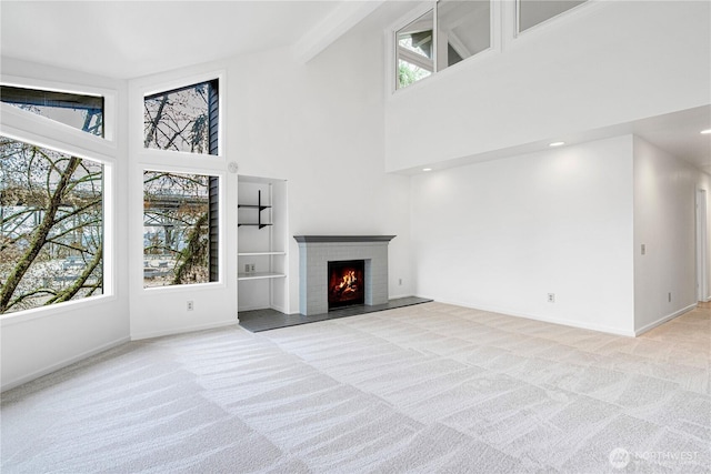 unfurnished living room with light colored carpet, baseboards, a brick fireplace, and a towering ceiling