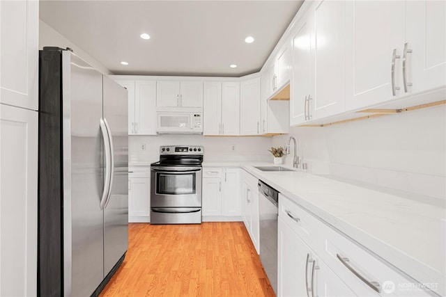 kitchen with white cabinets, light wood-style flooring, stainless steel appliances, and a sink