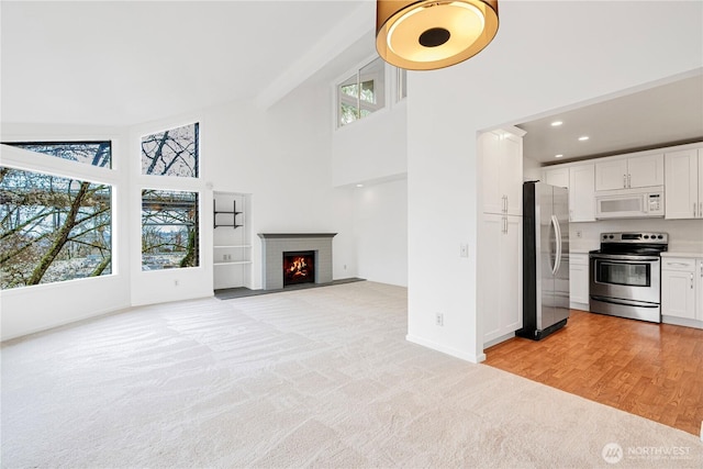 unfurnished living room featuring high vaulted ceiling, light carpet, baseboards, a brick fireplace, and recessed lighting