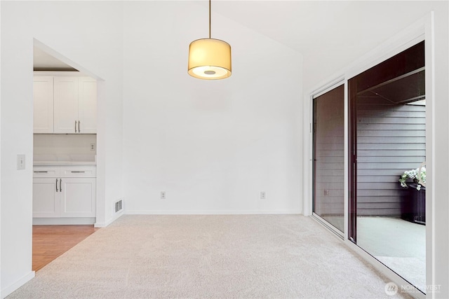unfurnished dining area with baseboards and light colored carpet