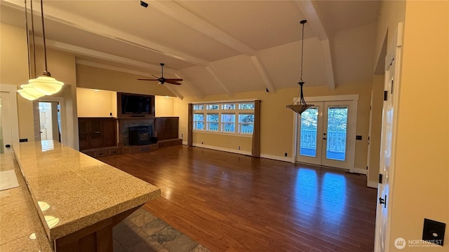 unfurnished living room with lofted ceiling with beams, dark wood finished floors, baseboards, a fireplace with raised hearth, and a ceiling fan