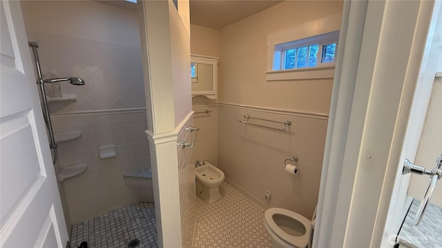 full bathroom featuring a shower stall, tile patterned floors, a wainscoted wall, toilet, and a bidet