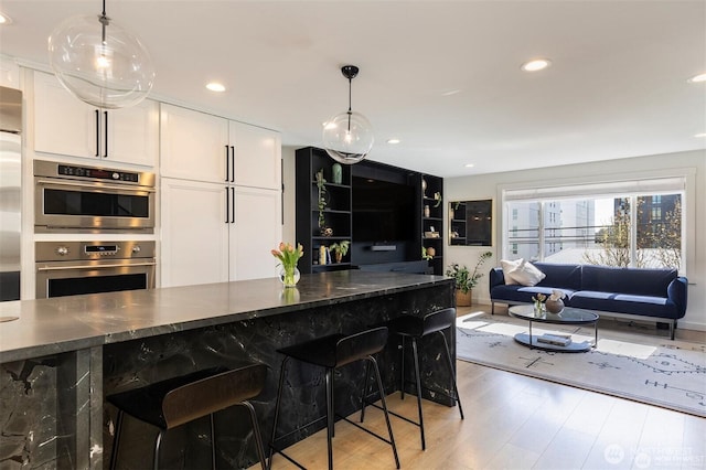 kitchen with appliances with stainless steel finishes, light wood finished floors, white cabinets, pendant lighting, and a breakfast bar area