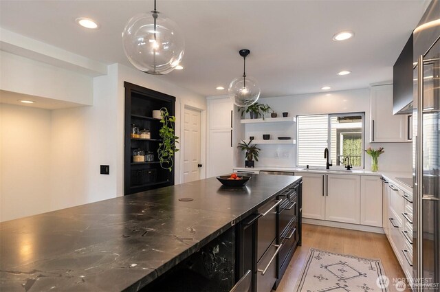 kitchen featuring open shelves, a sink, white cabinetry, light wood finished floors, and decorative light fixtures