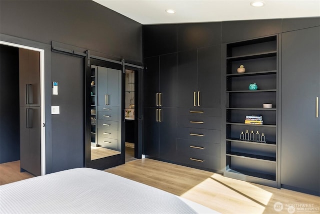 bedroom with light wood finished floors, recessed lighting, and a barn door