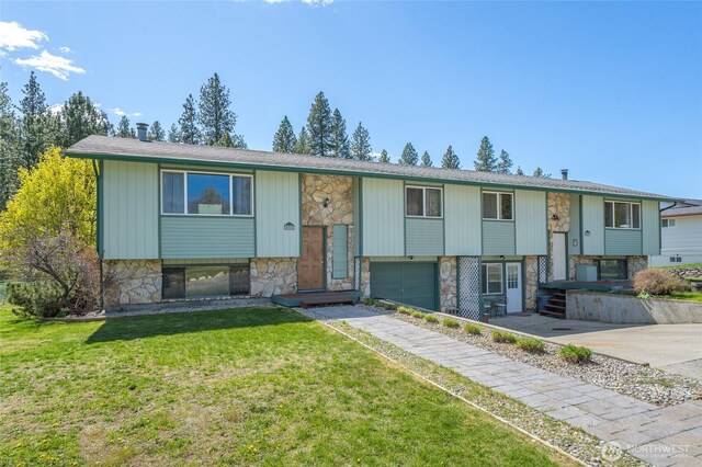split foyer home with an attached garage, stone siding, a front lawn, and driveway