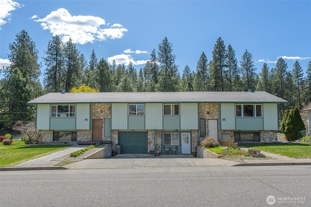 raised ranch with an attached garage, aphalt driveway, and stone siding