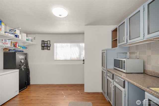 kitchen with open shelves, light wood-type flooring, white microwave, decorative backsplash, and washer / clothes dryer