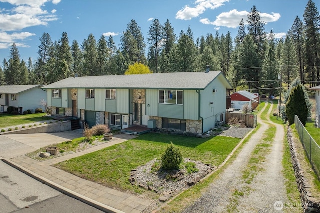 split foyer home with driveway, fence, stone siding, and a front yard