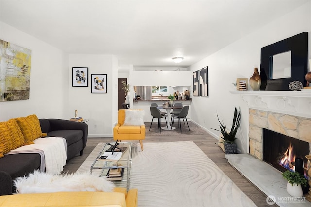 living room featuring a stone fireplace, baseboards, and wood finished floors