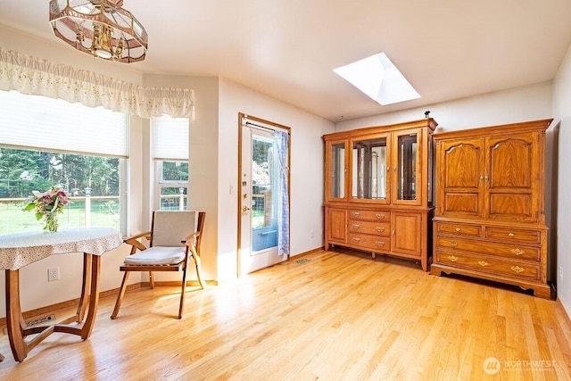 living area with a skylight, light wood-style flooring, baseboards, and a notable chandelier