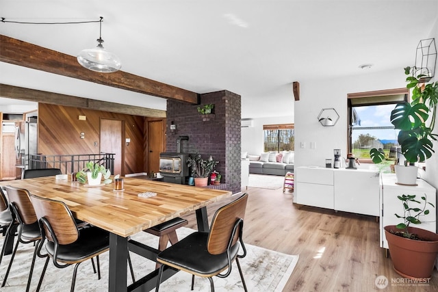 5752 Ronnie Hill Ln, Ferndale, WA 98248 - dining space featuring light wood-type flooring, wood walls, beam ceiling, and a wood stove